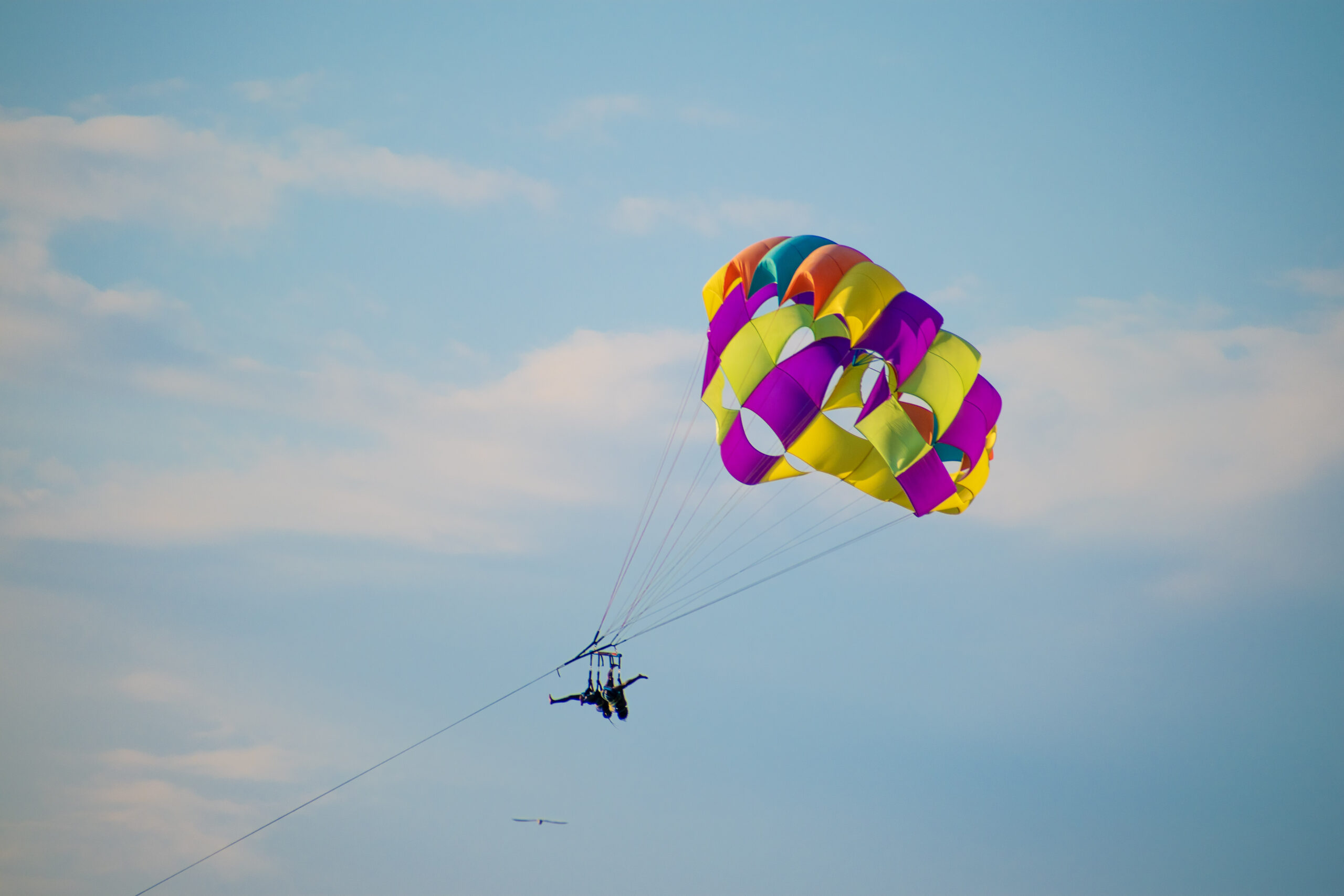 The tourist parasailing with the help of security in the cloudy sky on a sunny day